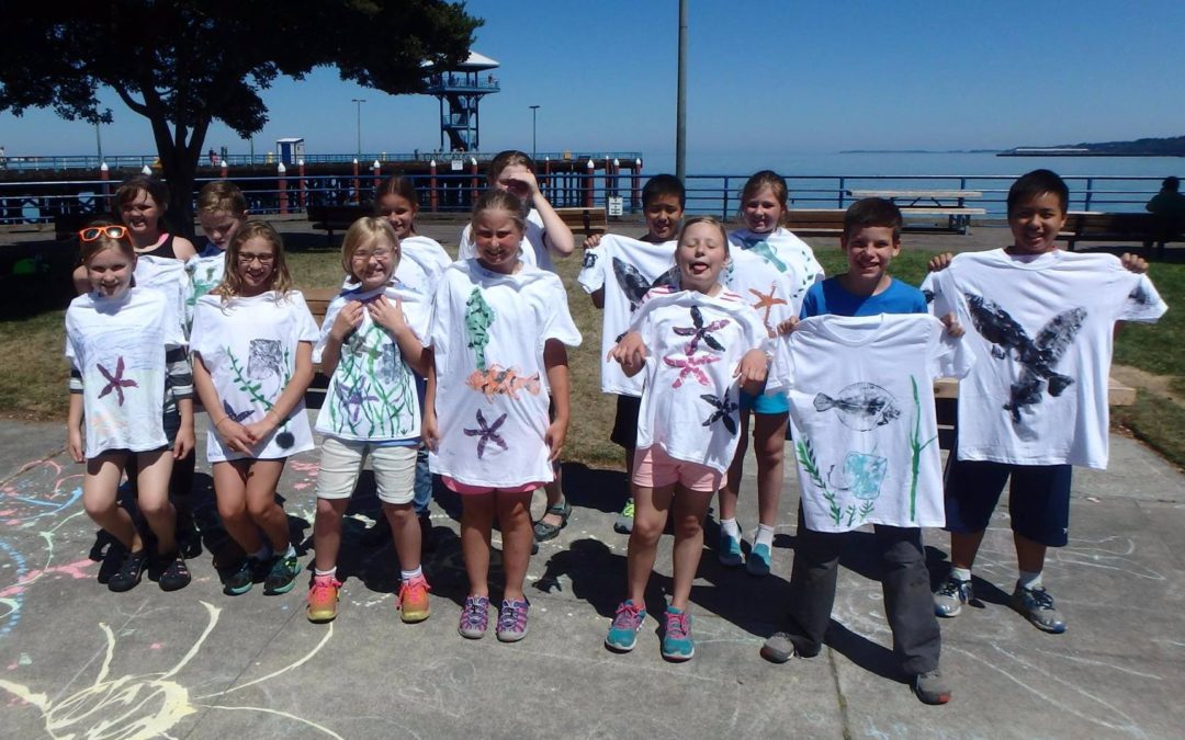 children standing in rows holding up tshirts with marine life designs